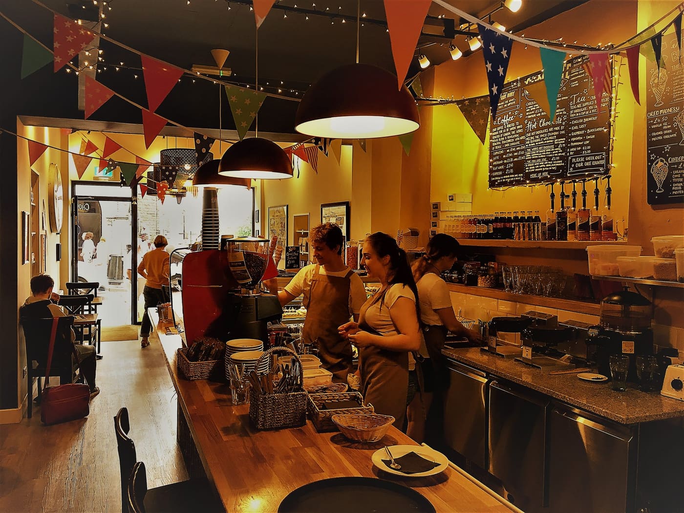 Inside the shop &mdash; warm lights, hanging bunting, chalkboard menus on the back wall, and the open kitchen counter where the chocolate is made.